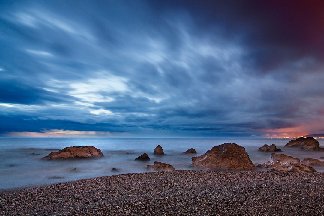 rocks at seashore under clouds